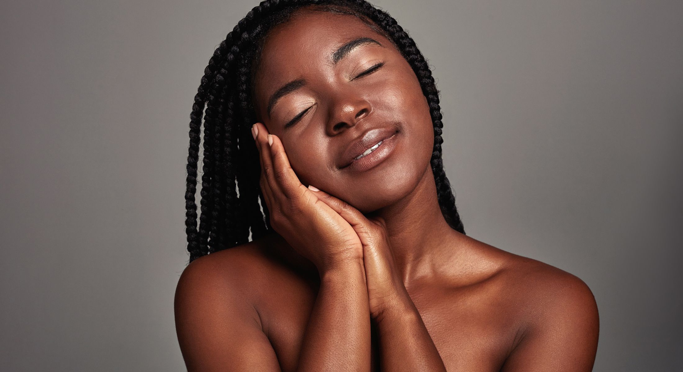 Woman with braids smiling and embracing herself.