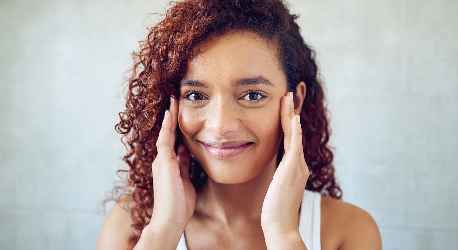 Smiling woman touching her face with hands.